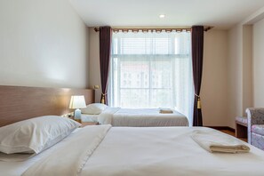 Hotellihuone, jossa on kaksi sänkyä, yöpöytä lampun kanssa, tuoli ja suuri ikkuna, jossa on verhot.