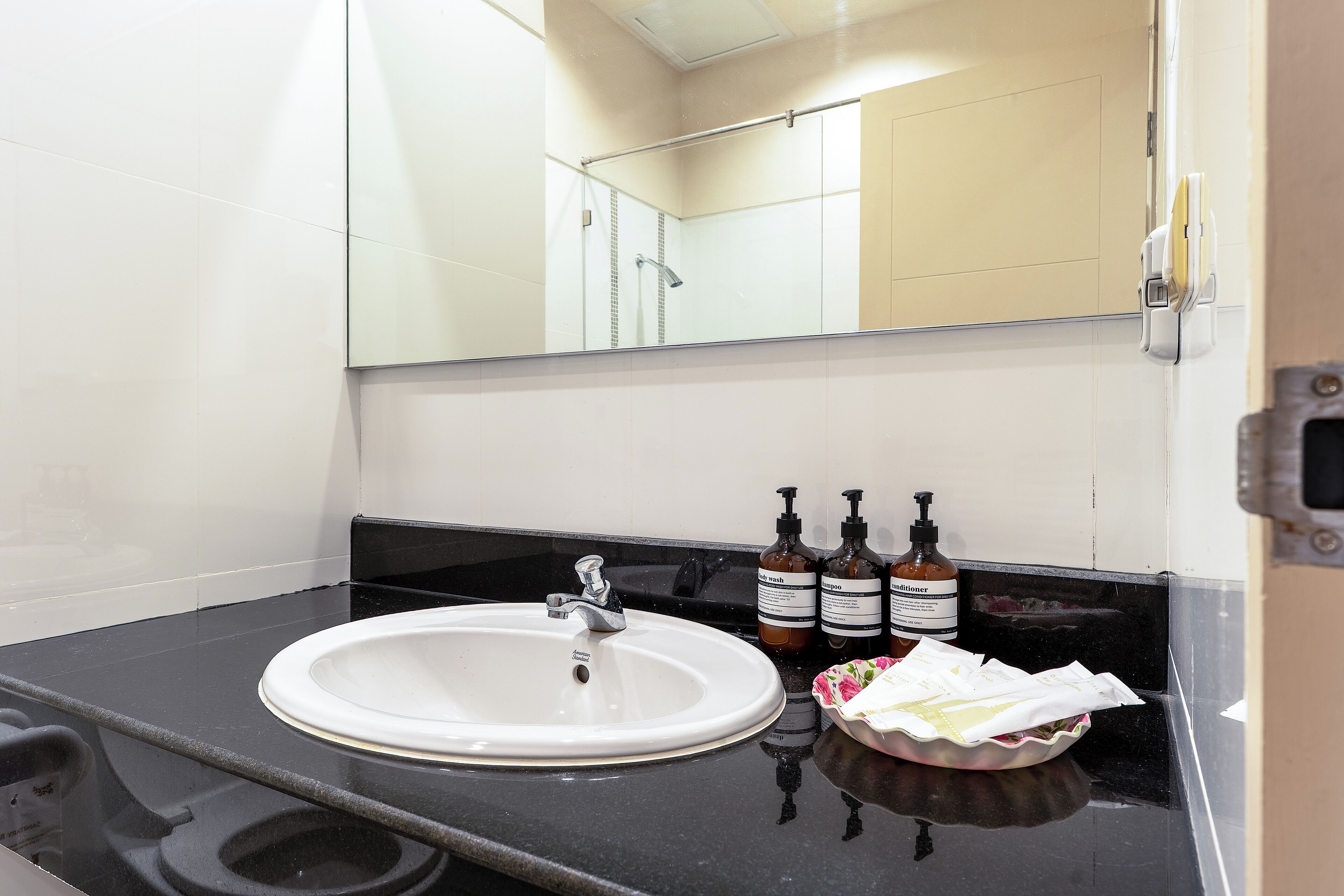 A bathroom with a white sink, black countertop, and a mirror above it. There are three bottles of hand soap and a tissue box on the counter.
