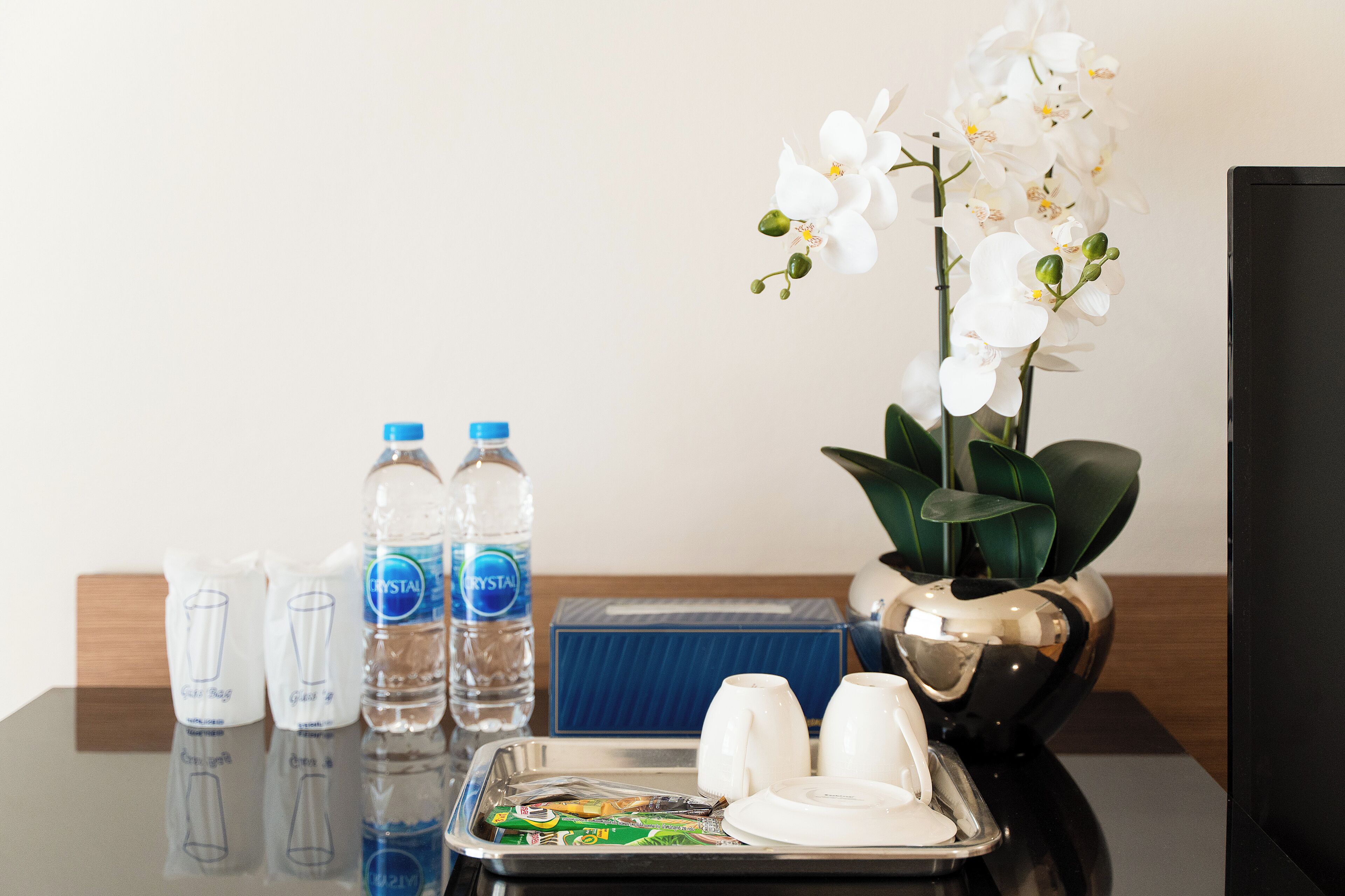 A hotel room with a tray table, water bottles, a vase with white orchids, and a blue box.