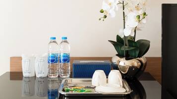 A hotel room with a tray table, water bottles, a vase with white orchids, and a blue box.