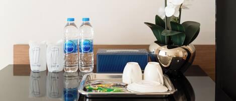 A hotel room with a tray table, water bottles, a vase with white orchids, and a blue box.