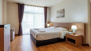 A hotel room with a bed, bedside table, lamp, and a painting on the wall. - Mahachai Grand View (Nakhon Si Thammarat)