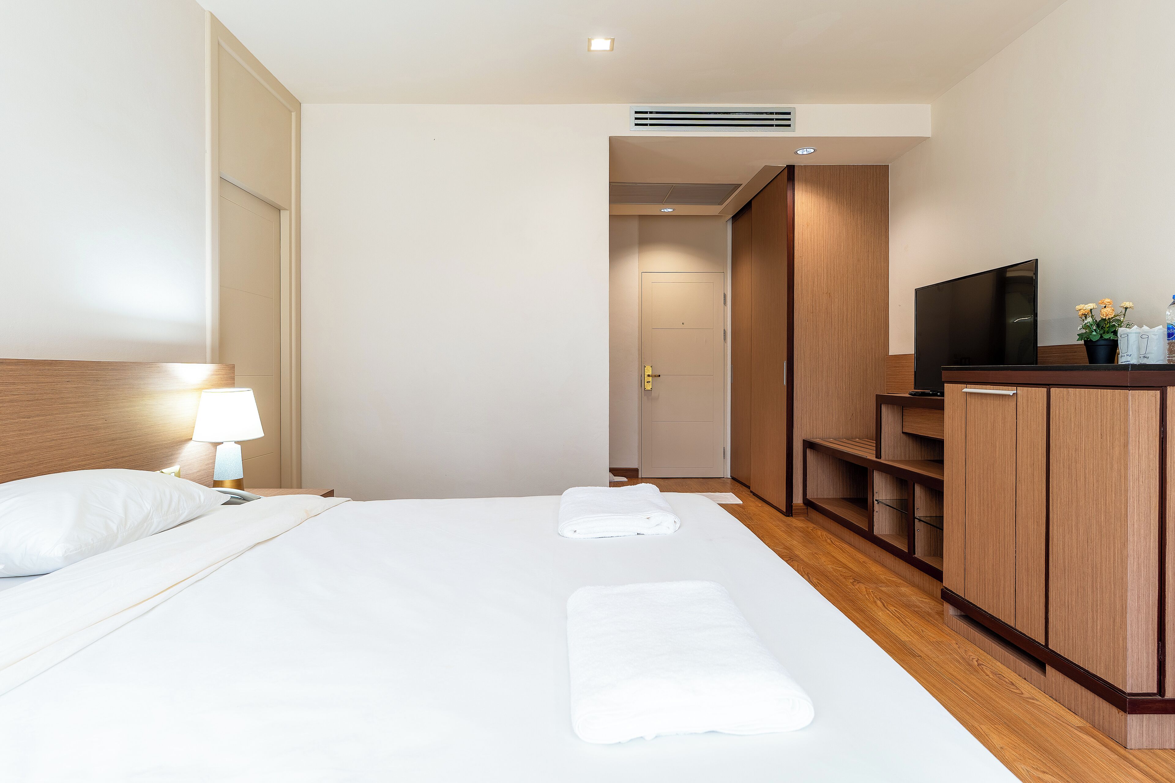 A hotel room with a bed, a TV, a desk with a lamp, and a wardrobe.