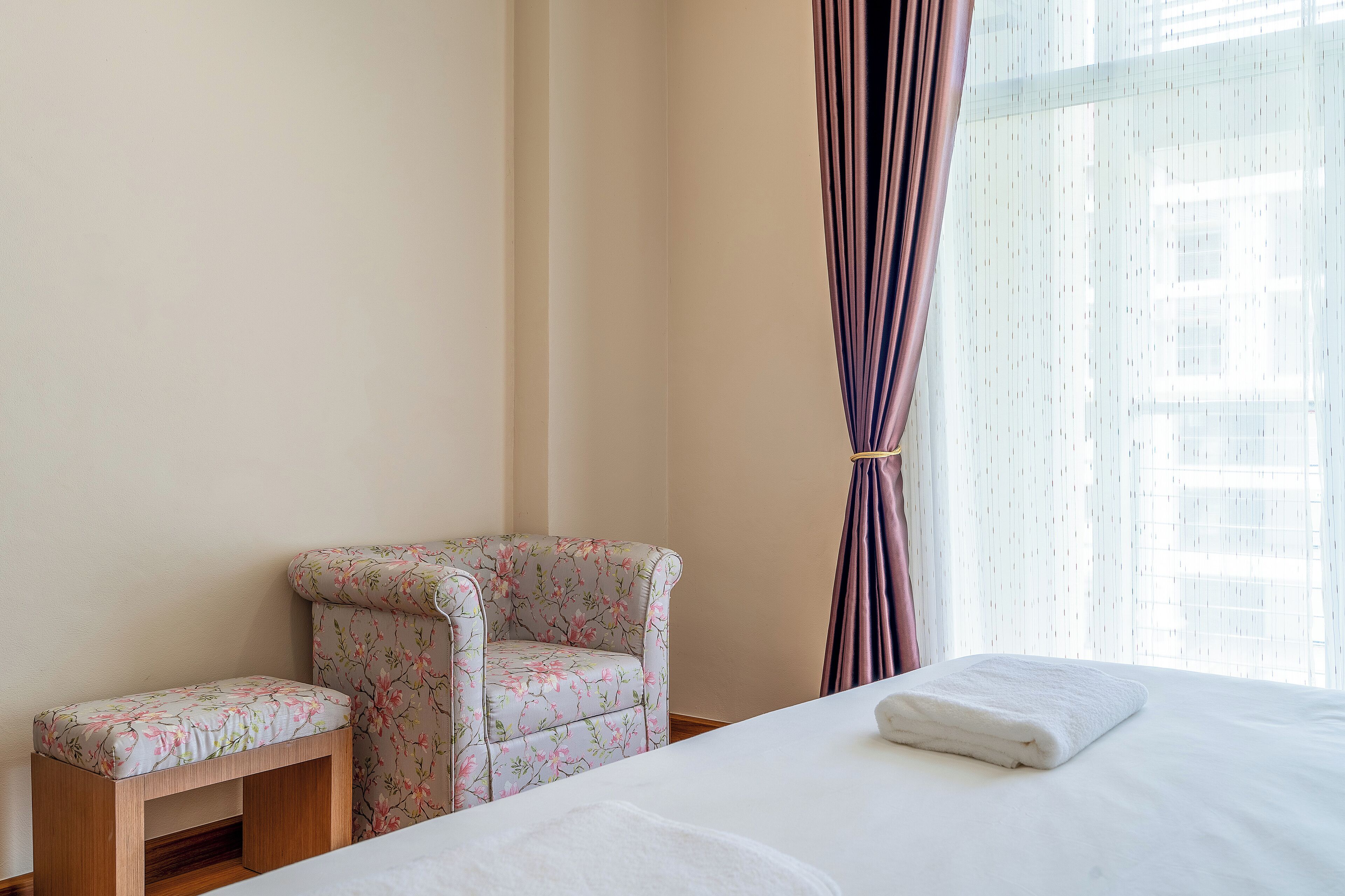 Una habitación de hotel con una cama, un pequeño banco y un sillón floral.
