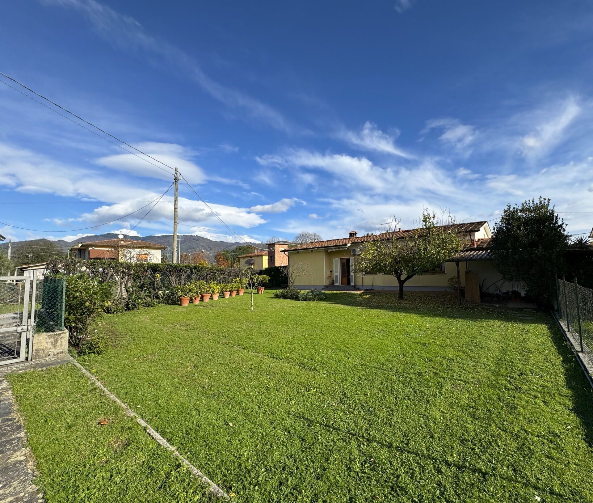 Une propriété résidentielle dotée d’une pelouse bien entretenue, d’un petit jardin agrémenté de plantes en pot et surplombée d’un ciel bleu dégagé.