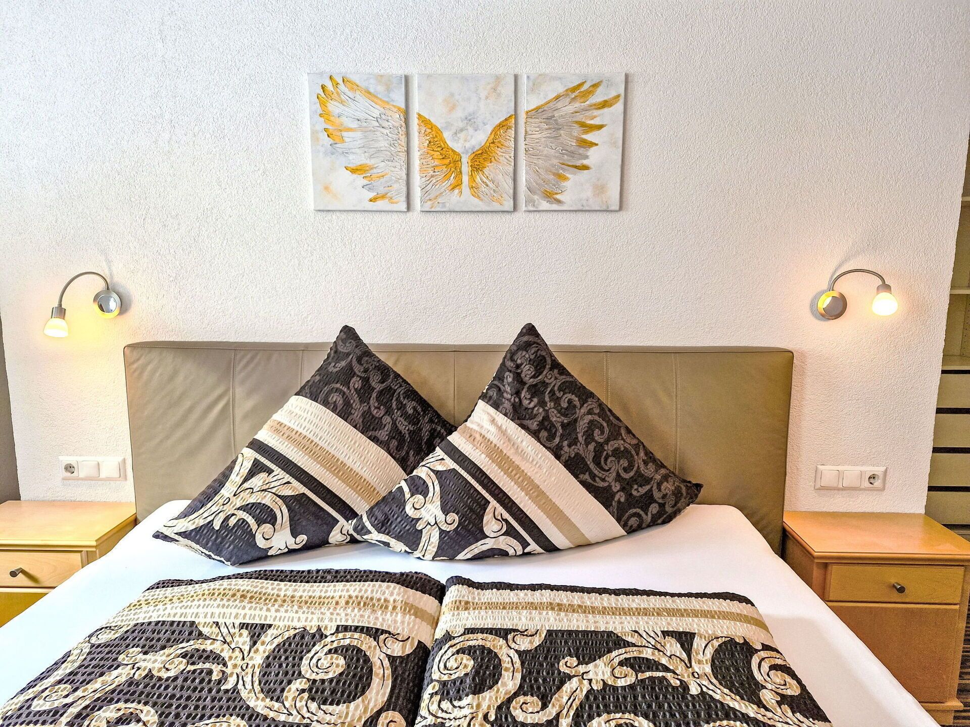 Una habitación de hotel con cama, dos mesitas de noche y lámparas fijadas a la pared.