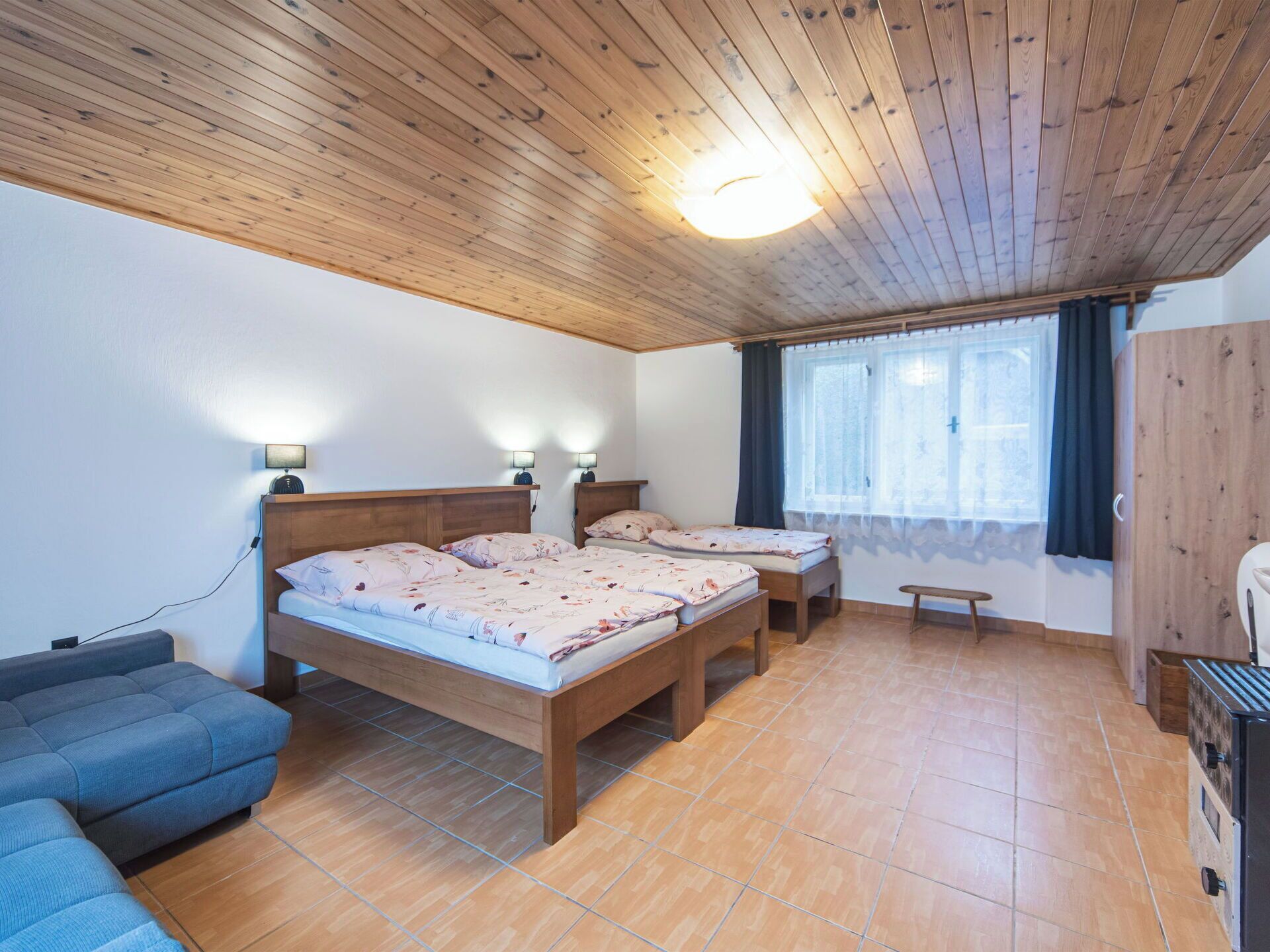 A room with two wooden beds, a sofa, a window with curtains, and a wooden wardrobe.