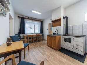 A compact kitchen with a dining area, wooden cabinets, a built-in oven, and a window with curtains.