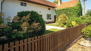 Une maison blanche avec un toit recouvert de tuiles rouges, une clôture en bois et un jardin bien entretenu.