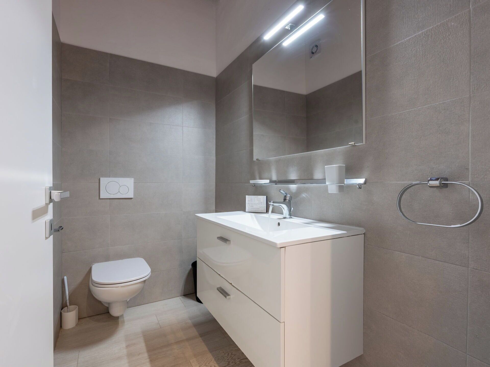 Een moderne badkamer met een wit wastafel, spiegel en toilet.