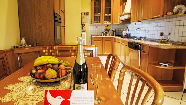 Une table à manger avec une bouteille de champagne, un saladier de fruits et une carte de bienvenue.