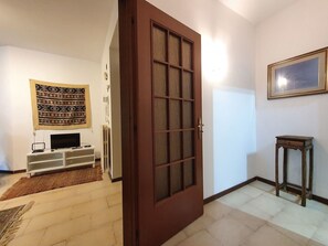 A room with a wooden door, a television on a stand, a patterned tapestry on the wall, and a small table.