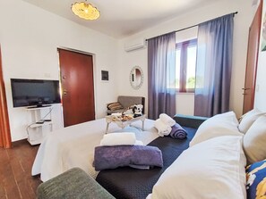 Ein Hotelzimmer mit einem Bett, einem Fernseher, einem kleinen Tisch mit Wasserkocher, einer Couch und einem Fenster mit Vorhängen.