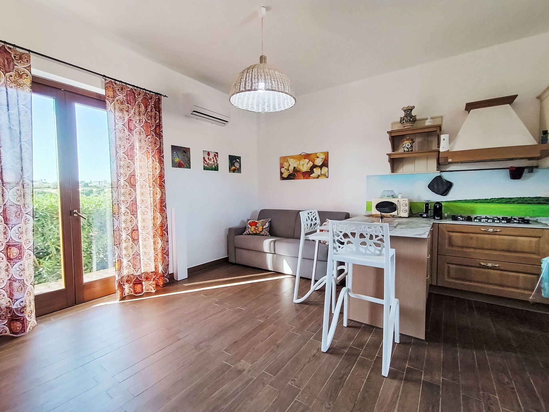 A modern kitchen with a dining area, a sofa, and a view of greenery outside.