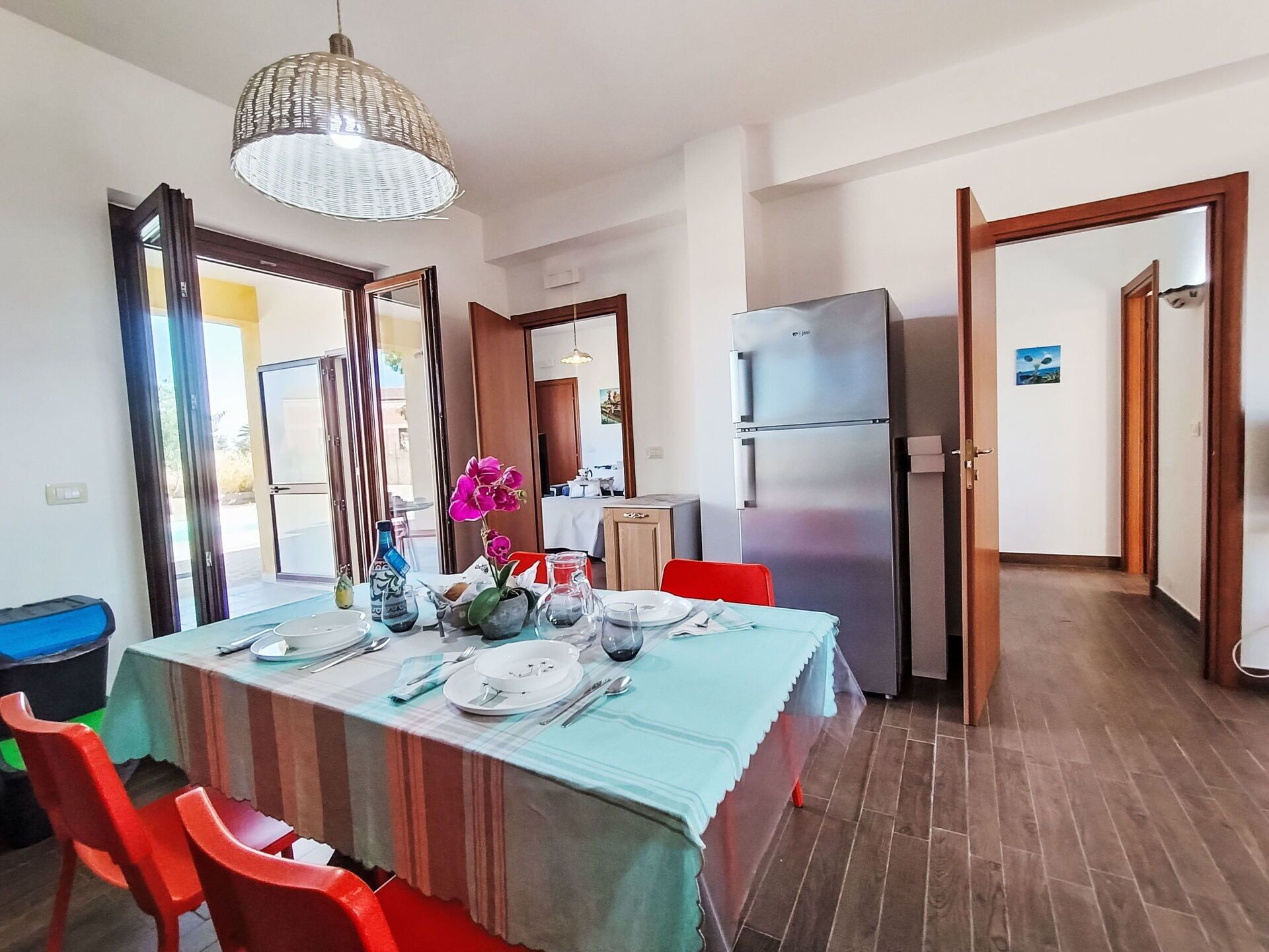 A dining area with a table set for four, a refrigerator, and a view of the outside.