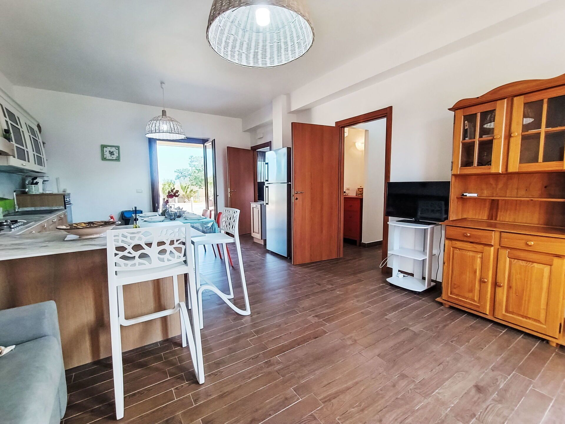 A spacious kitchen with wooden cabinets, a dining area with a white chair, and a large window.