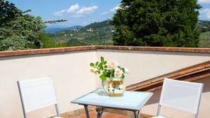 A terrace with two white chairs and a small table with a vase of flowers. The terrace overlooks a scenic landscape with trees and distant hills. - Cosy apartment for 6 guests with pool, WIFI, A/C, TV and pets allowed, close to Florence (Impruneta)