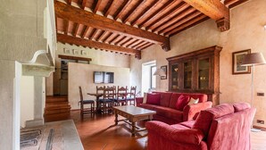 A spacious living room with a wooden ceiling, a red sofa set, a dining table with chairs, and a cabinet with glass doors. - Cosy apartment for 6 people with WIFI, A/C, pool, TV and pets allowed, close to Florence (Impruneta)