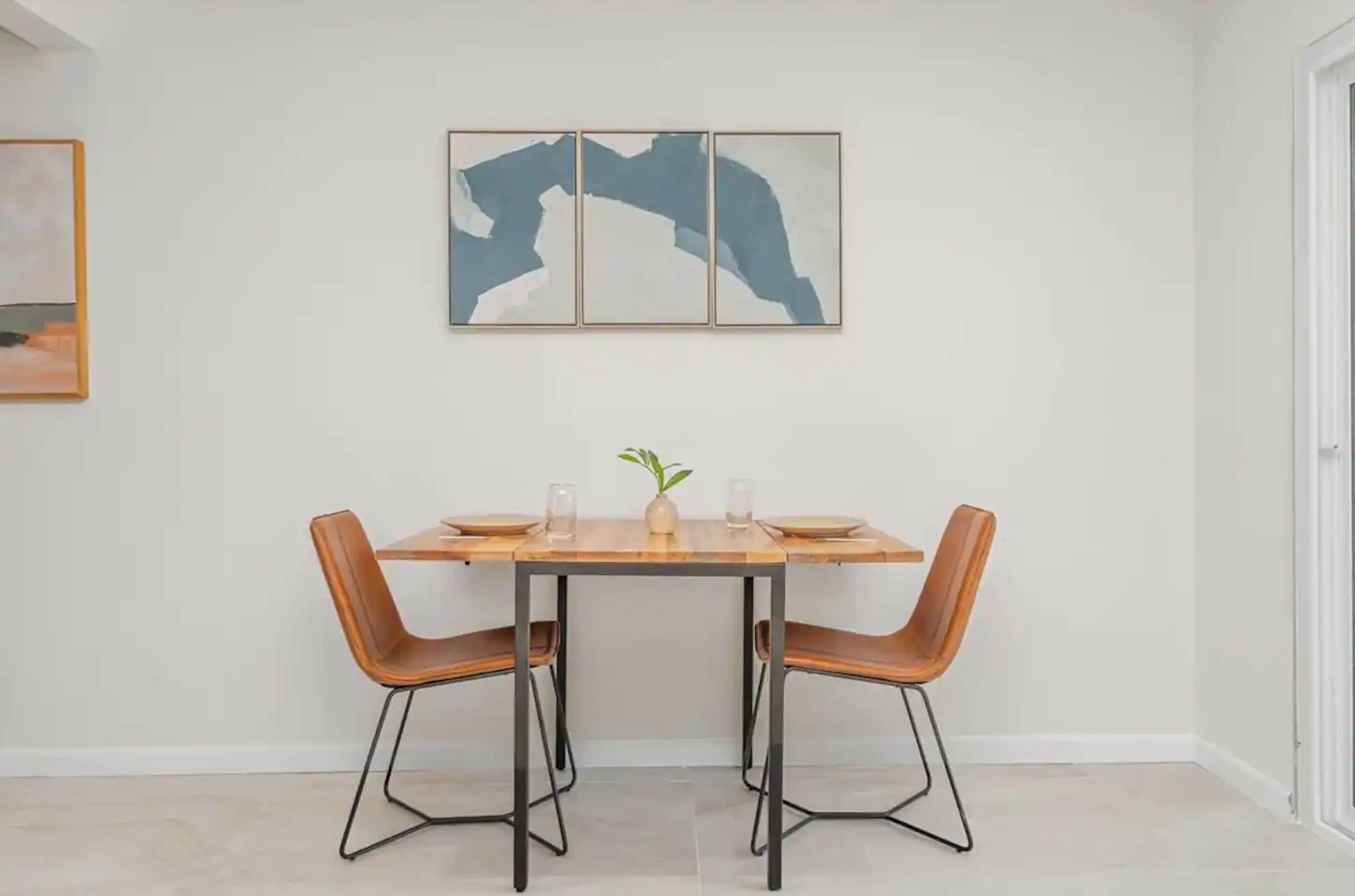 Un comedor con una mesa rectangular, dos sillas y un florero con una planta.