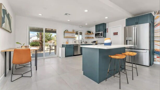 A modern kitchen with a central island, bar stools, and a dining area with a table and chairs.