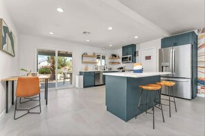 Een moderne keuken met een centraal eiland, barkrukken en een eethoek met een tafel en stoelen.