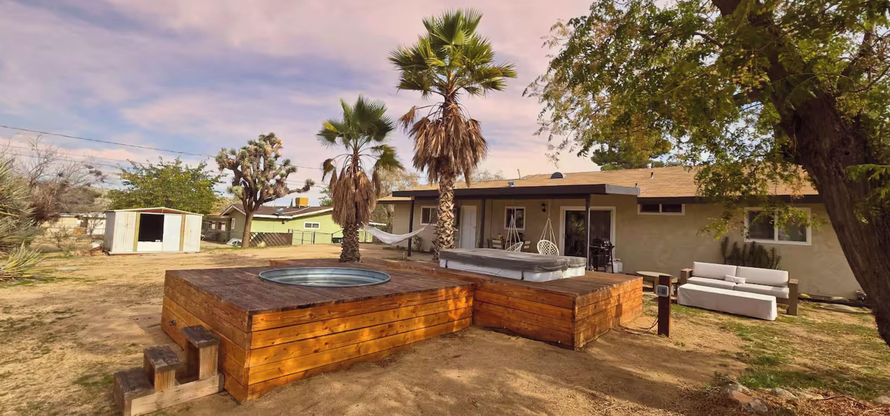Patio trasero con jacuzzi de madera, una hamaca y zona de estar con sofá.