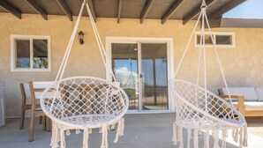 Two white macrame hanging chairs with fringes, a wooden table, and a wooden bench.