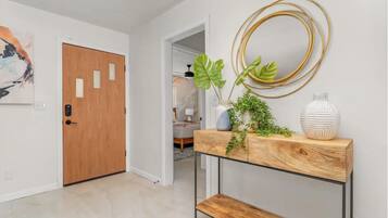 A hallway with a wooden door, a console table with plants, and a wall-mounted circular mirror.