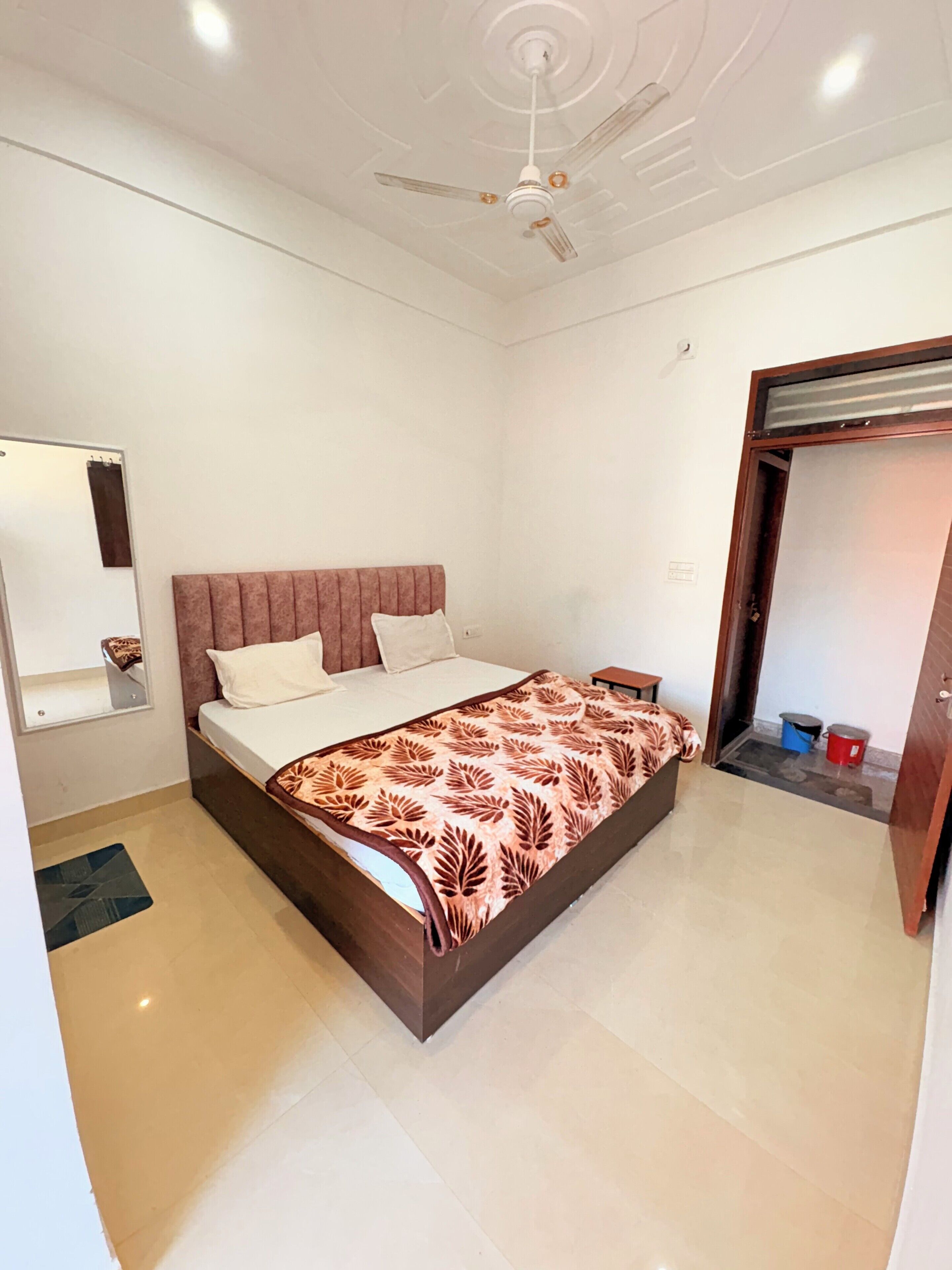 A bedroom with a bed, a ceiling fan, a mirror, and a small table.