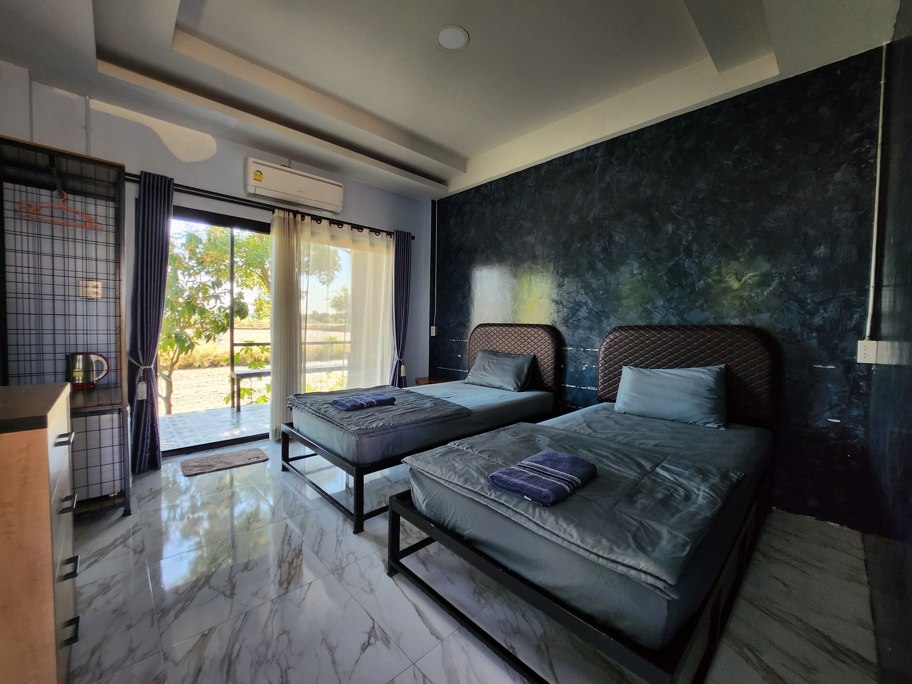 A modern bedroom with two beds, a large window with curtains, a marble floor, and a wall-mounted air conditioner.