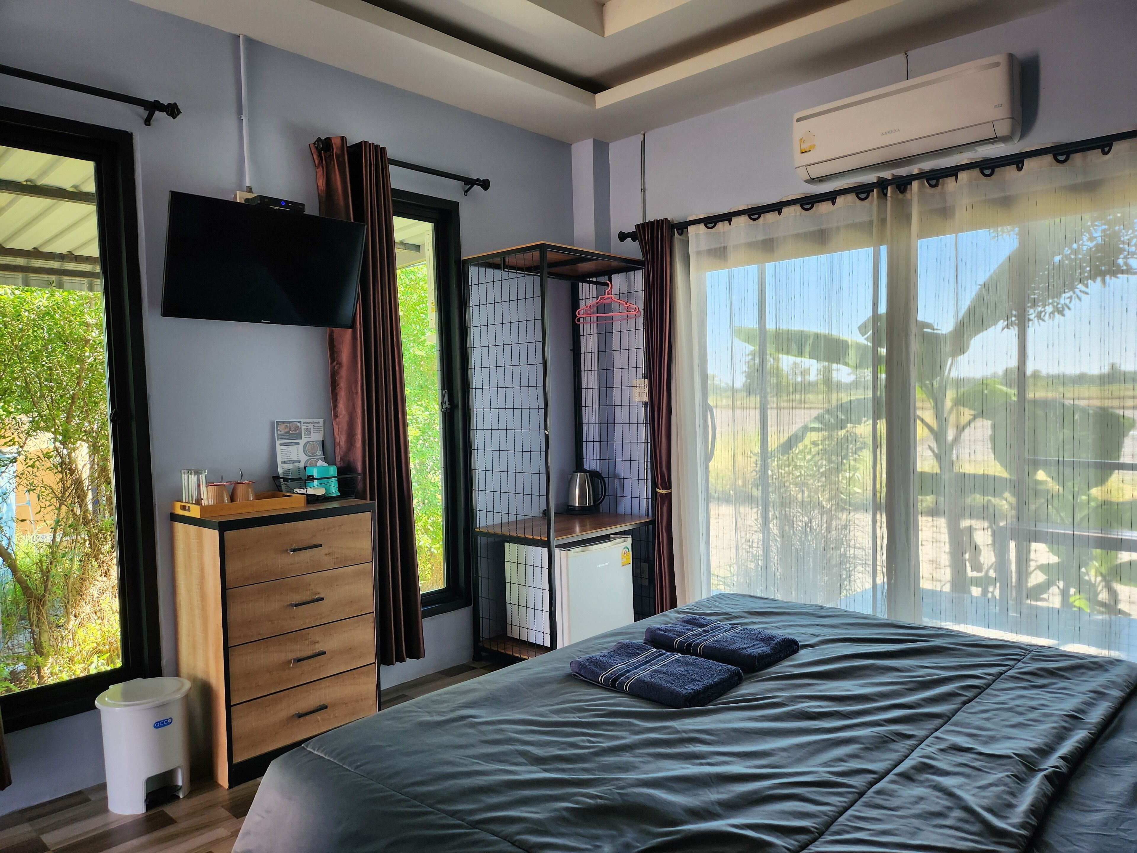Un dormitorio con cama, televisor, armario, una mesita y ventana con cortinas.