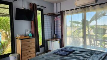 Un dormitorio con cama, televisor, armario, una mesita y ventana con cortinas.