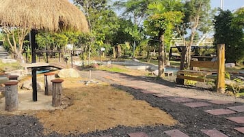 A thatched-roof structure with a bench and a small pool area, surrounded by trees and a paved walkway.