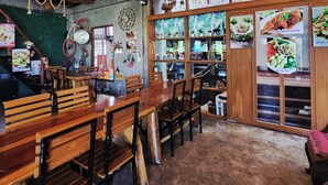 Un interior de restaurante con mesas y sillas de madera, decoraciones colgantes y pizarras con el menú.