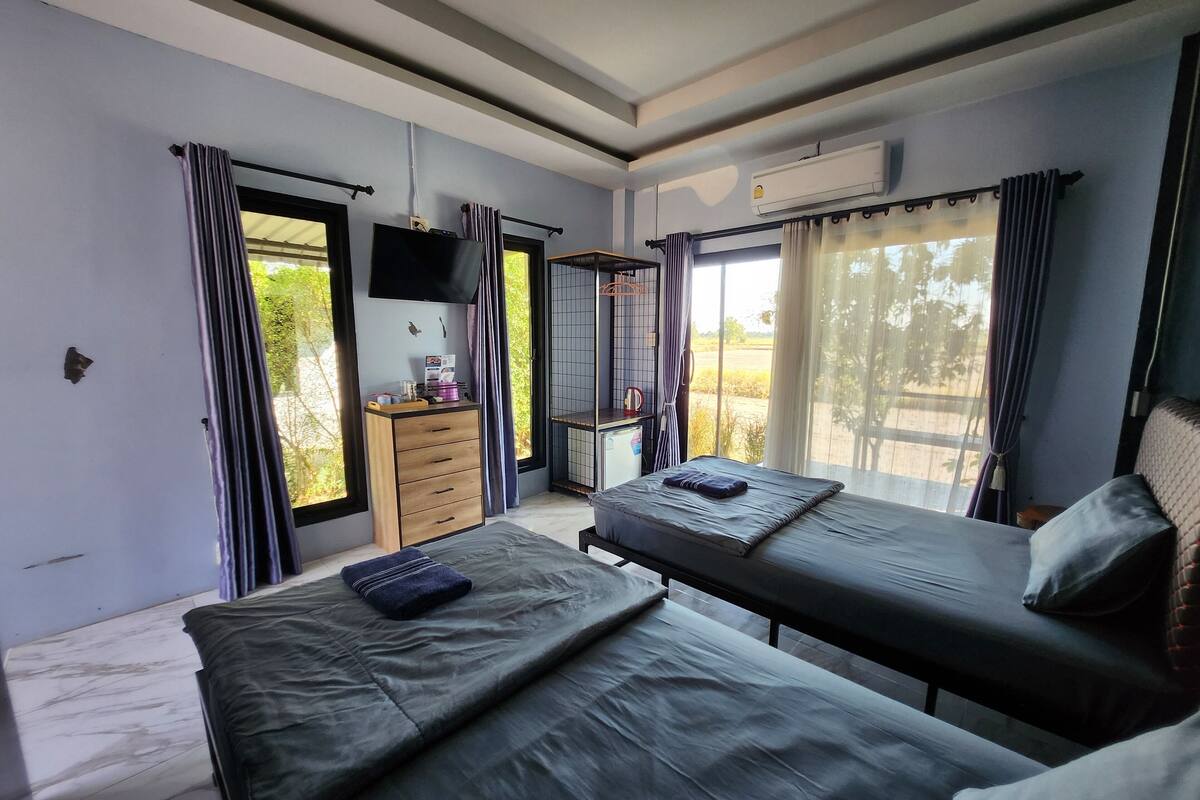 A room with two beds, a TV, a small cabinet, and a window with curtains.