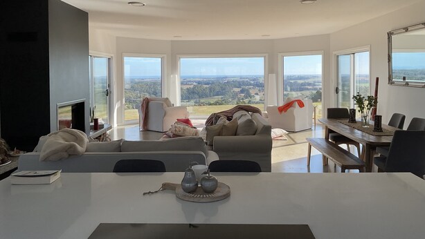 A modern living room with a large window, a fireplace, and a dining area with a view of the countryside.