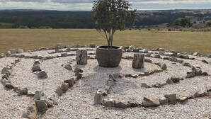 A circular stone arrangement with a central tree, surrounded by a grassy field and a distant landscape.