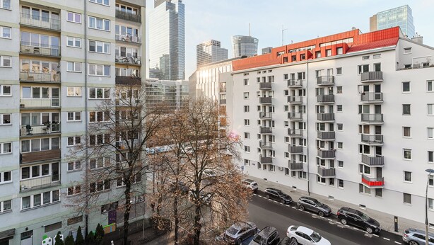 A multi-story residential building with balconies, a parking lot, and modern high-rise buildings in the background. - Lumina apartment for family in Warsaw (Warsaw)