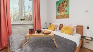 A bedroom with a bed, a bedside table with a lamp, a window with curtains, and a painting on the wall. - Lumina apartment for family in Warsaw (Warsaw)