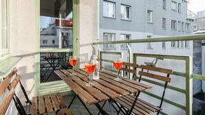 A balcony with wooden tables and chairs, two glasses of red wine, and a view of a building with multiple windows. - Lumina apartment for family in Warsaw (Warsaw)