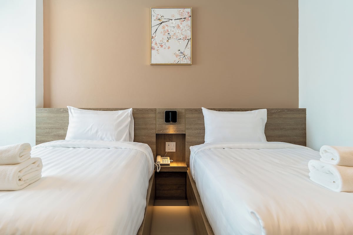 Een hotelkamer met twee bedden, witte lakens, een houten hoofdeinde, een nachtkastje met een telefoon en een kunstwerk aan de muur.