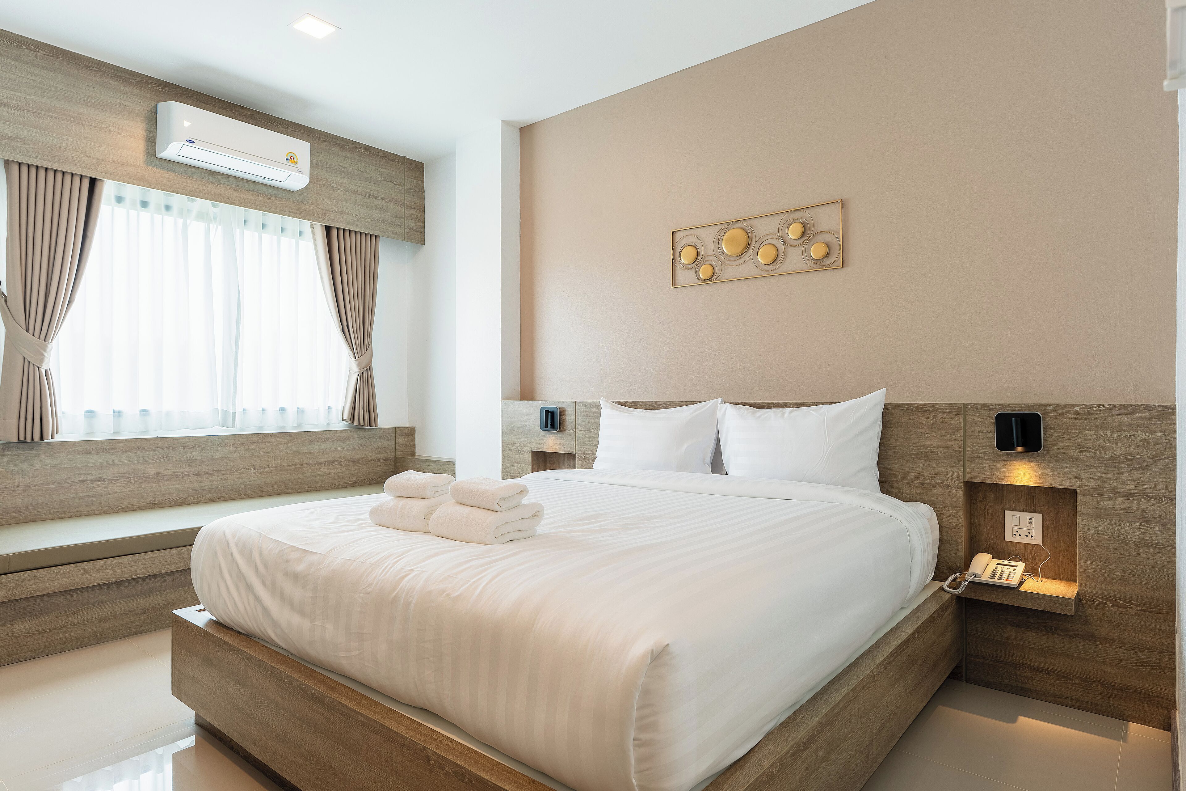 Une chambre d’hôtel moderne dotée d’un grand lit, d’une banquette intégrée, d’une table de chevet avec un téléphone et d’un climatiseur fixé au mur.