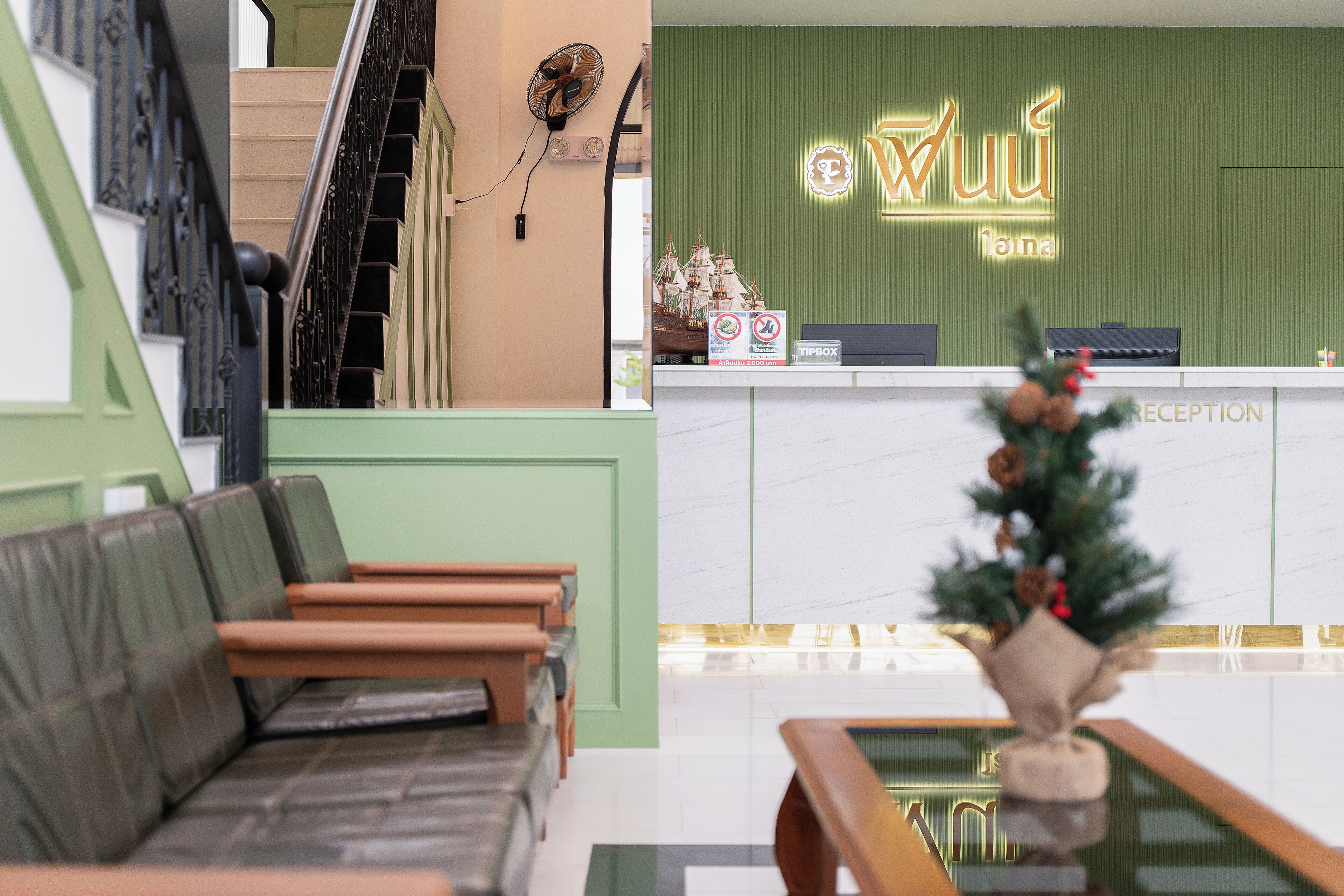 A hotel reception area with a green wall, a reception desk, and a small Christmas tree.