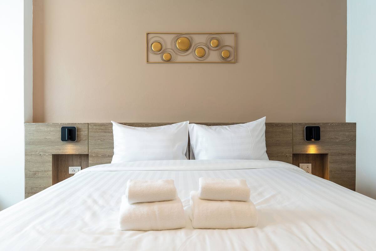 Een net opgemaakt bed met witte lakens en twee opgevouwen handdoeken aan het voeteneinde.