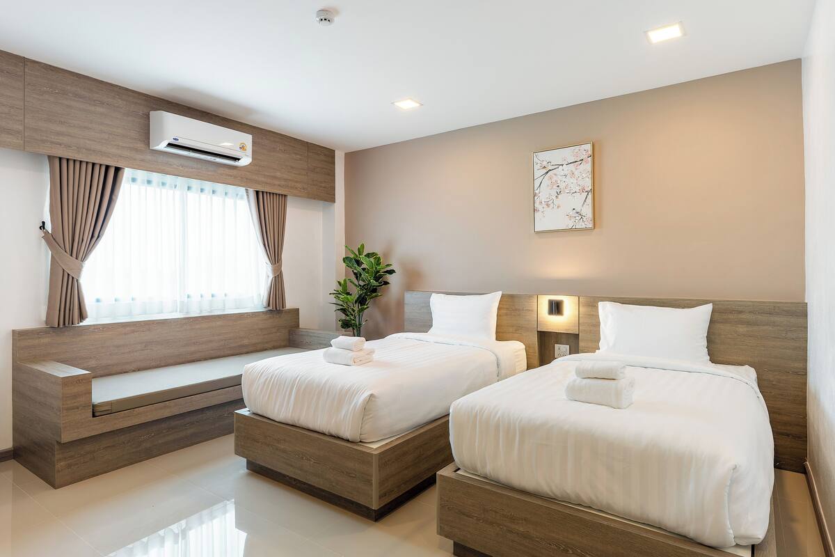 Een moderne hotelkamer met twee bedden, een inbouwbank, een airconditioning, een potplant en een wanddecoratie.