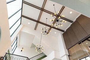 Um interior moderno com teto alto, luminárias geométricas e escada com corrimão verde.