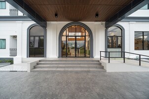 Entrada de um edifício moderno com um grande arco, degraus que levam a ele e teto de madeira.
