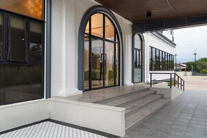 Uma entrada de edifício com um conjunto de degraus que levam a uma porta, uma área coberta com teto de madeira e chão de azulejos.