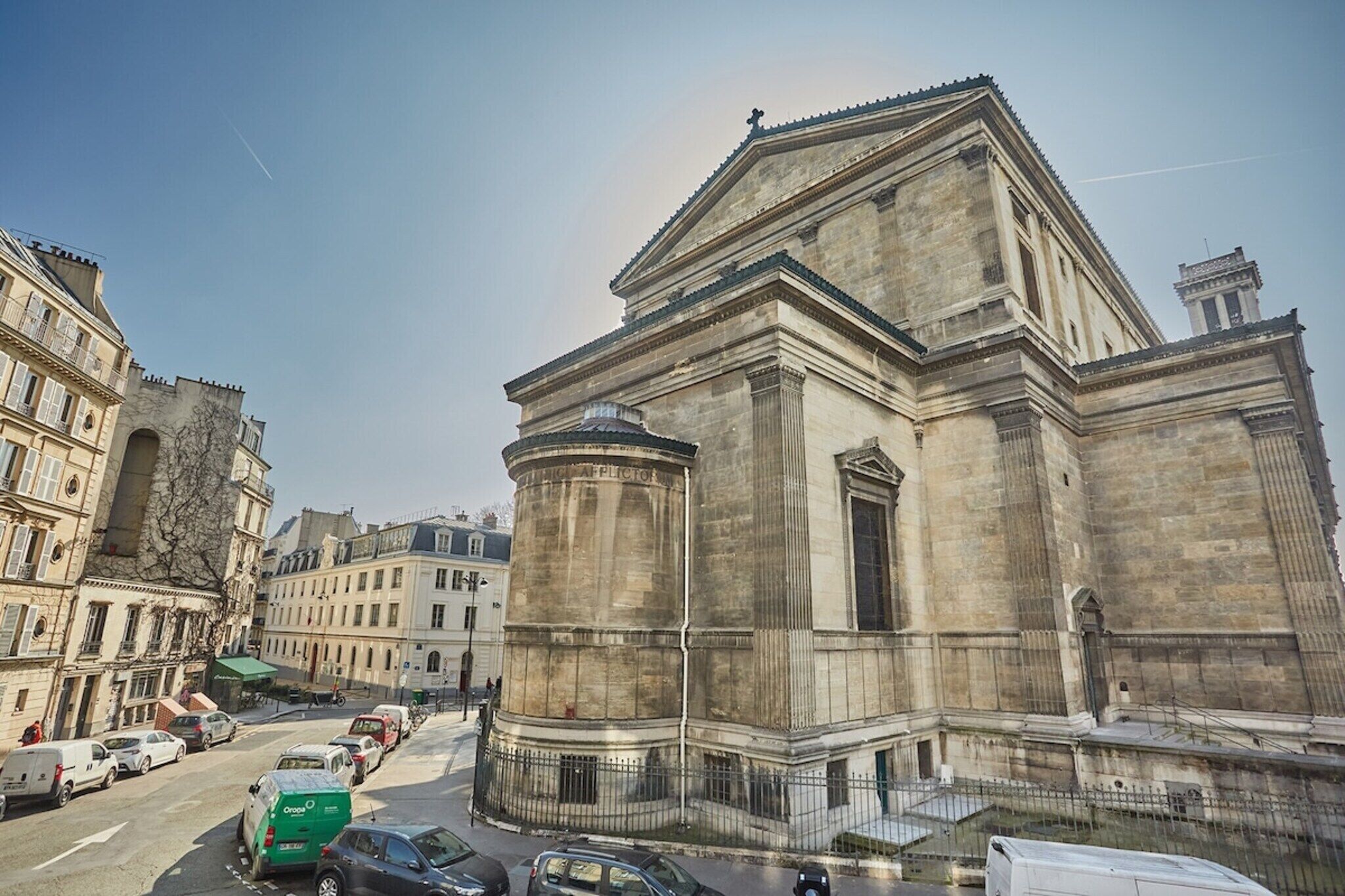 A historic building with classical architecture, including a prominent dome and columns, situated in a city street with parked cars and other buildings.