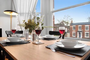 A dining table set with white bowls, plates, and cutlery, with two glasses of red wine and a vase of white flowers. - WhiskAwayStays - St Stephens Court - Apartment 3 (Worcestershire)